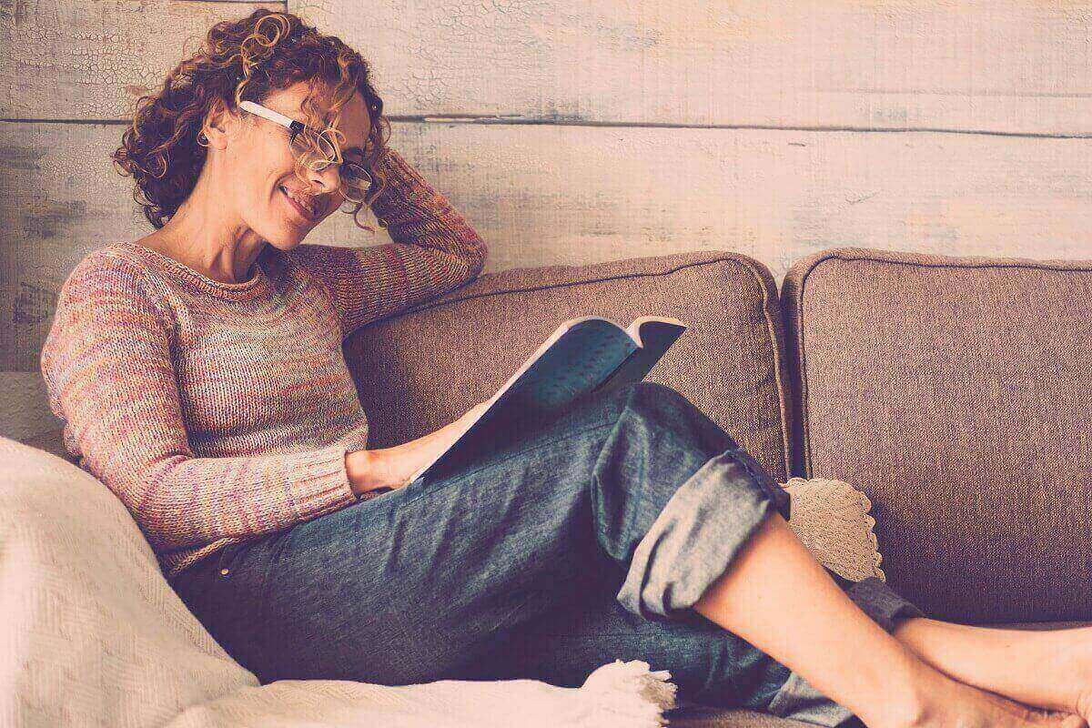 Kobieta po 50-tce czytająca książkę na łóżku.