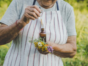 Starsza babcia na podwórku trzyma zioła.