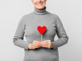 Starsza kobieta stoi i trzyma patyk z naklejonym czerwonym sercem.